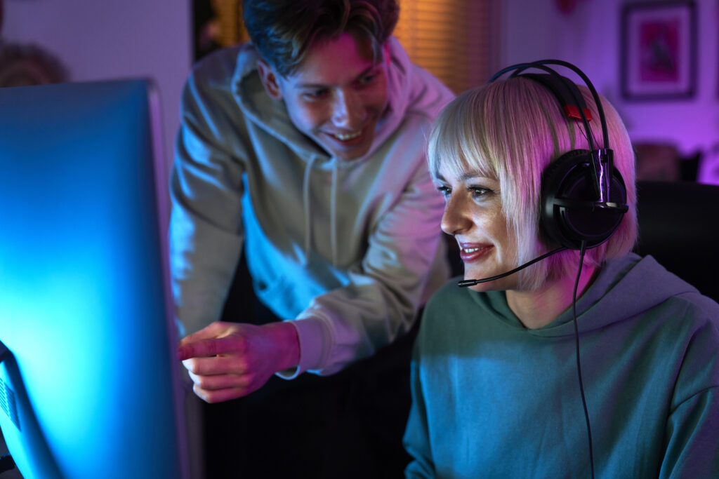 Caucasian woman playing game at night on Desktop PC and her friend is supporting her